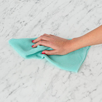 Hand holding a teal SEEP plastic-free cloth on a marble surface