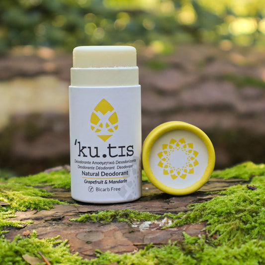 'ku.tis' natural deodorant Grapefruit & Mandarin essential oils fragranced. Bicarbonate of Soada free stick on a wooden log with a green, natural background