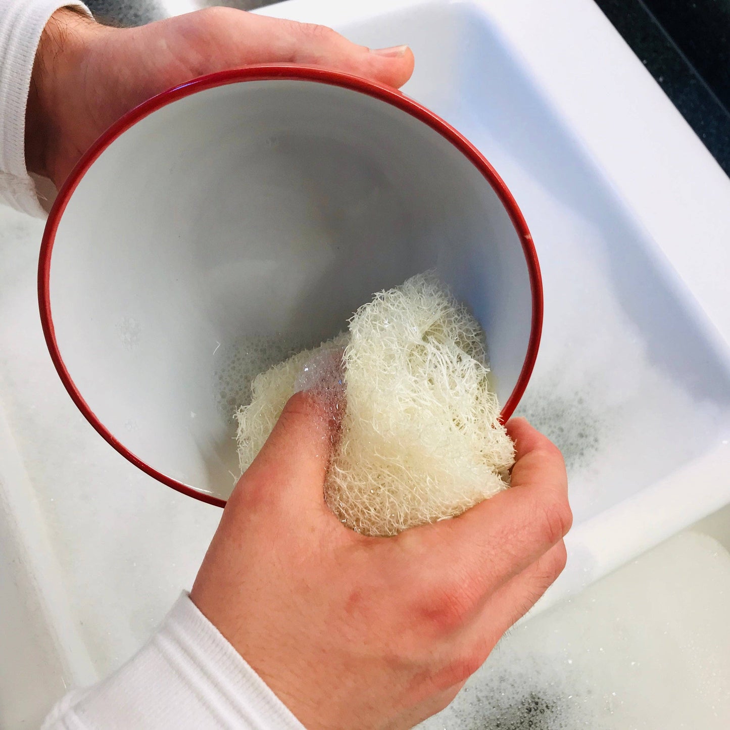 Person holding a red bowl with a microplastic-free loofah dish sponge inside, over a sink