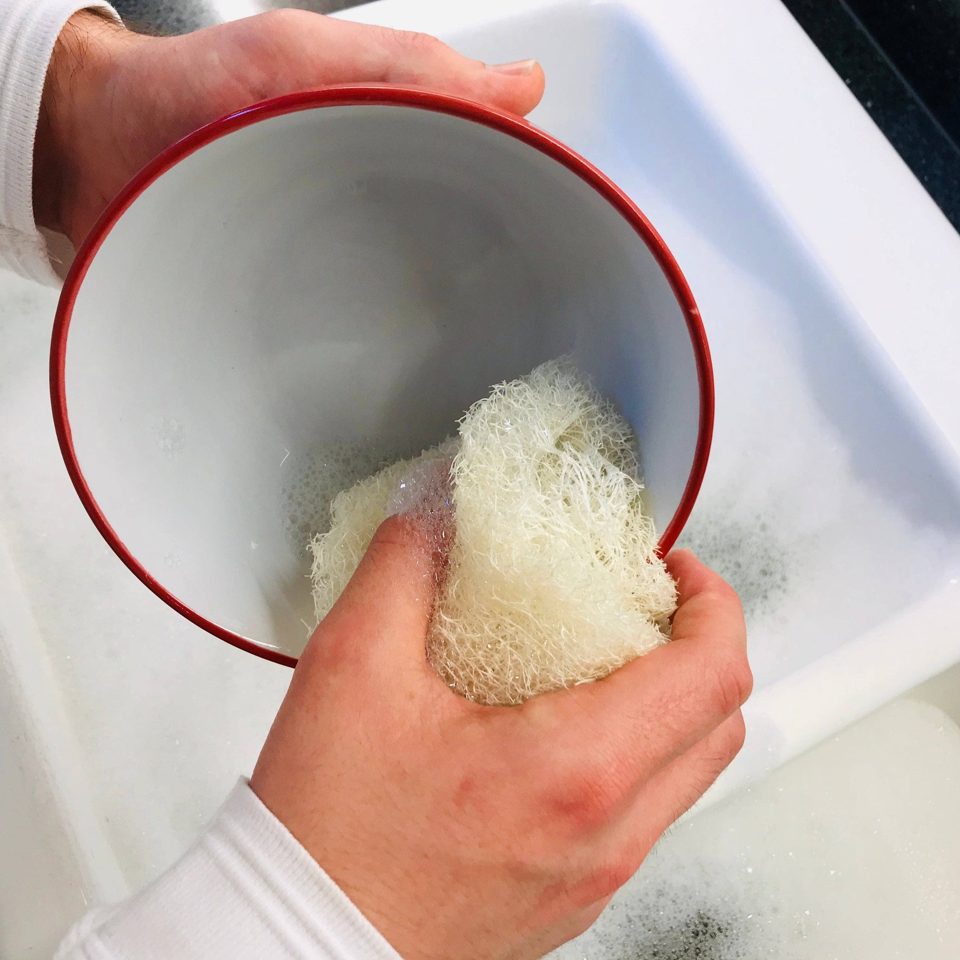Person holding a red bowl with a microplastic-free loofah dish sponge inside, over a sink