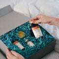 Person selecting a skincare bottle from a box filled with green crinkle paper