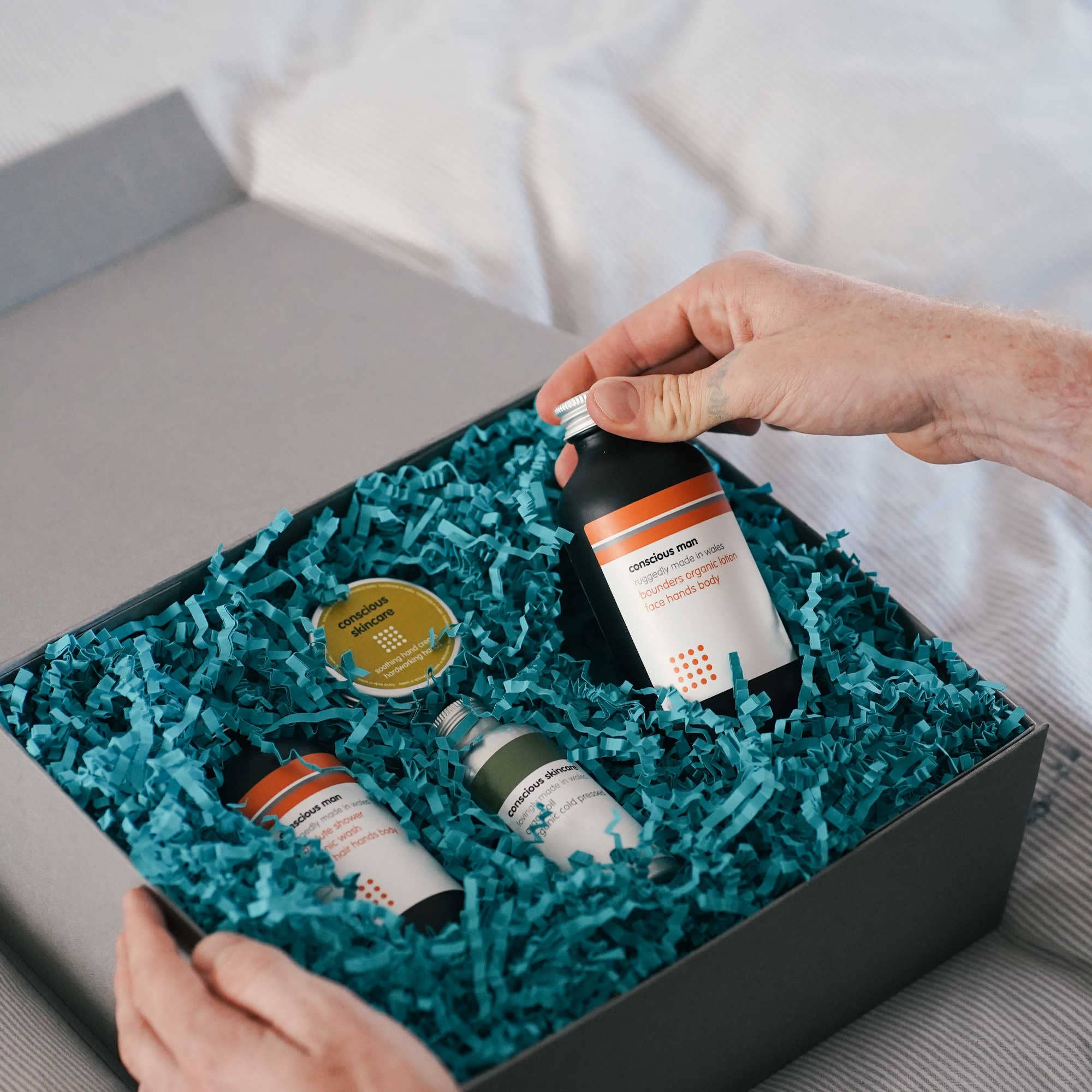 Person selecting a skincare bottle from a box filled with green crinkle paper