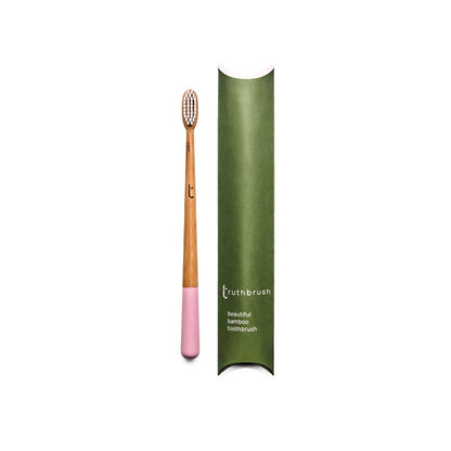 Pink handled plastic-free amboo toothbrush with pink base and green plastic-free packaging on a white background