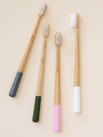 Four bamboo  handled toothbrushes with colored handles on a beige background