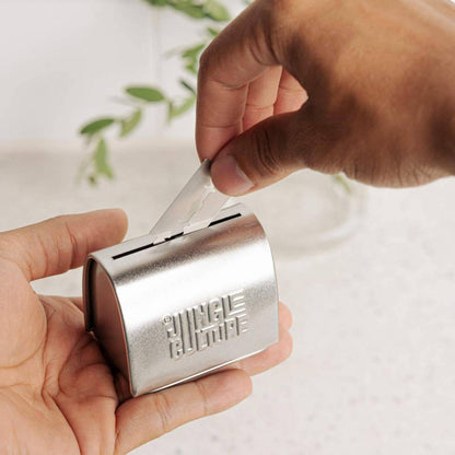 Hand holding silver tin with other hand dropping razor blade in slot of tin