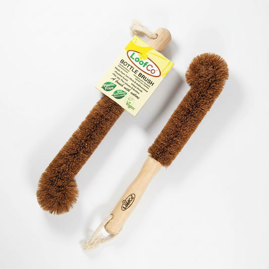 Two LooF Co. plastic-free vegan Bottle Brushes with brown bristles and light wood handles, one with its paper tag attached, set against a solid blue background.