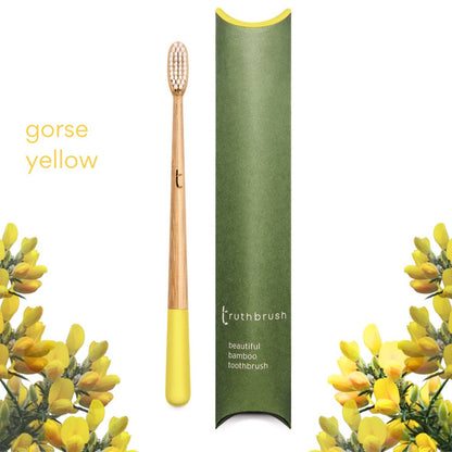 Yellow handled bamboo toothbrush with castor bean medium firmness bristles and green case, surrounded by yellow flowers, on a white background.