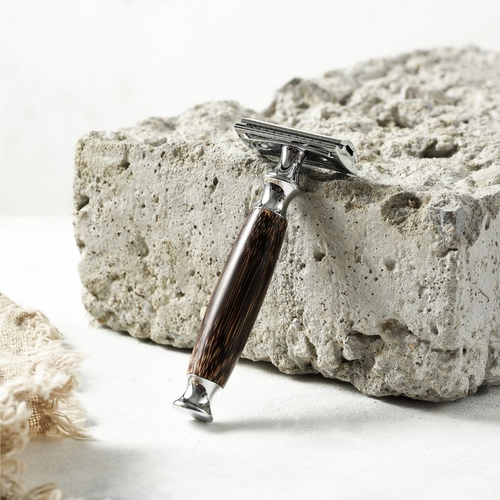 A vintage-style safety razor with a dark brown wood-grain handle and silver metal head, resting on a textured gray stone block.