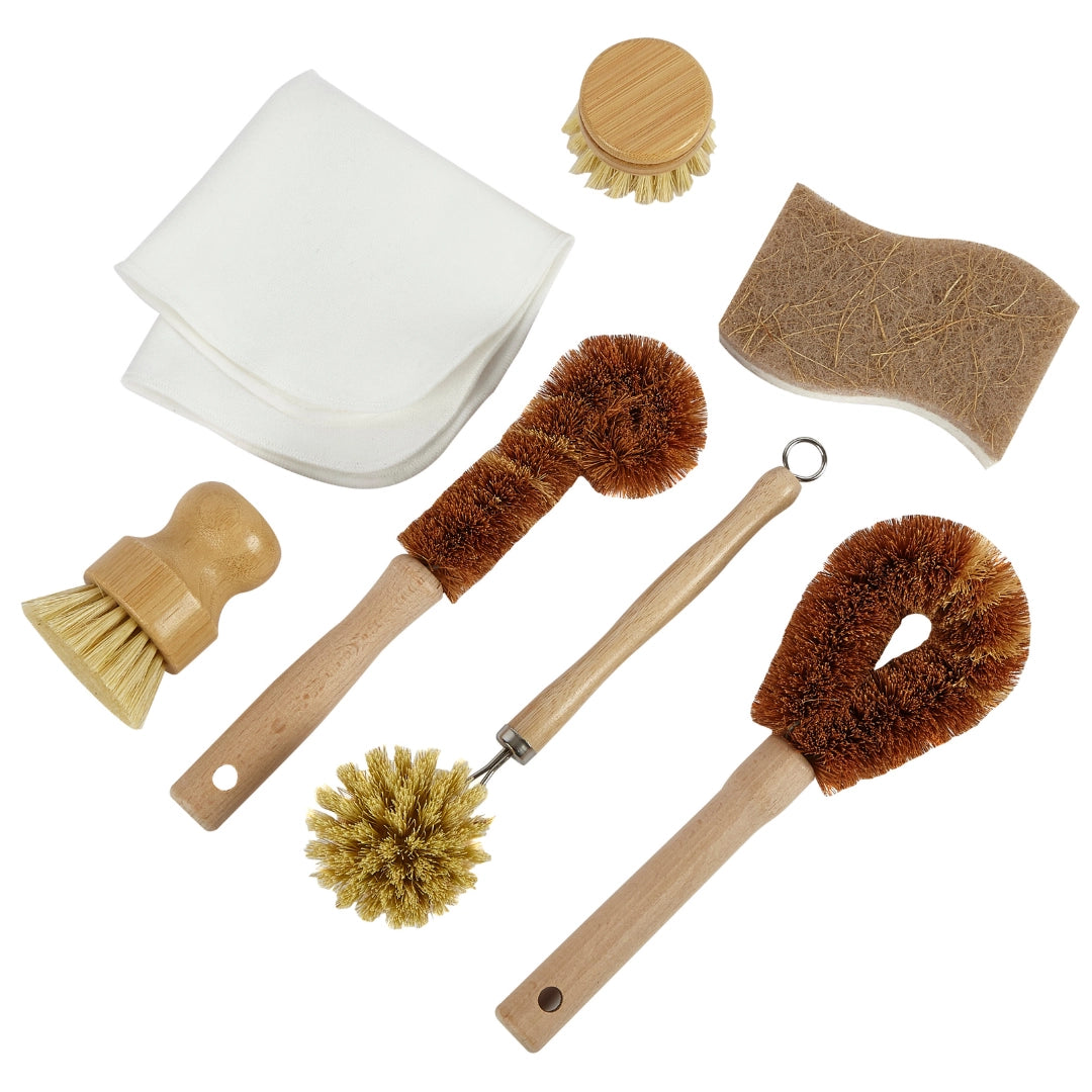 A 7-piece natural coconut scrubber set with wooden handles and natural brown coir bristles, including a body wash scrubber, a shoulder scrubber, a foot scrubber, a sponge, a cloth, and two small cleaning brushes, arranged on a white background.