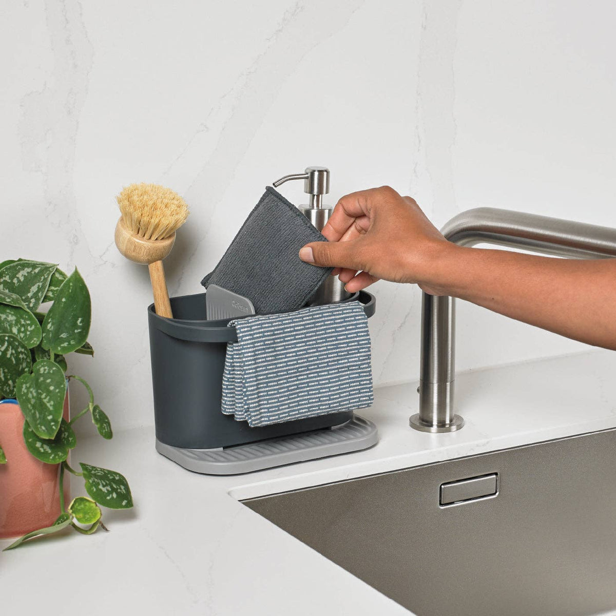 Person using a recycled plastic dish rack with a plant and sink in the background