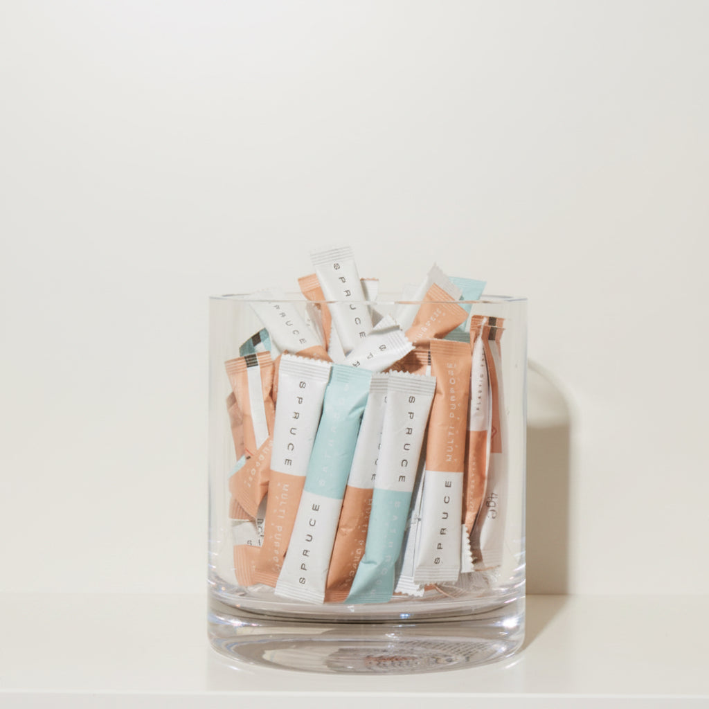 Clear glass container filled with small  compostable, plastic free, chemical free packets on a light background